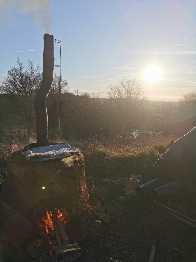 Four artisanal en bauge autoconstruit en pleine cuisson au bois de récupération, coucher de soleil, Atelier Élémen'terre Ariège